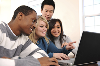 Cuatro estudiantes mirando una computadora portátil.